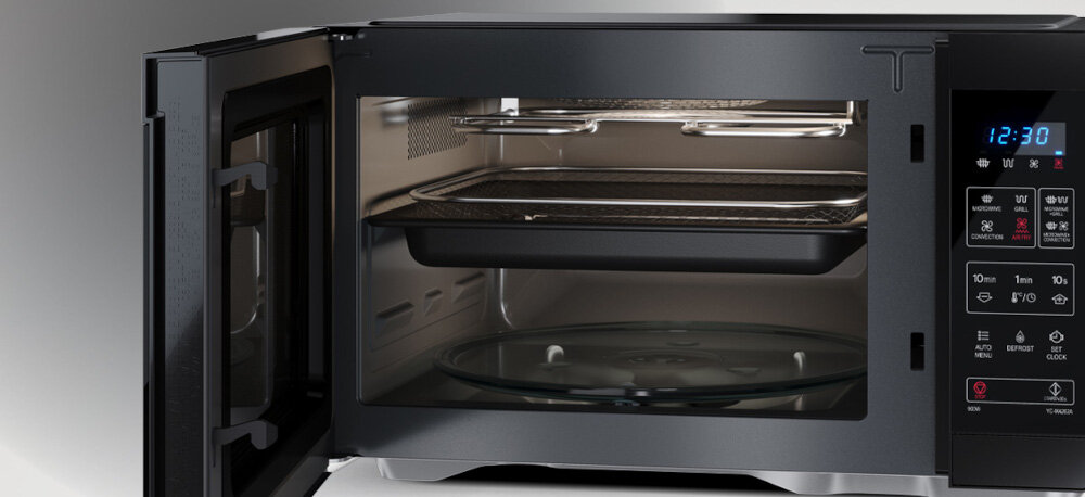 KUCHNIA MIKROFALOWA Z AIRFRY SHARP YC-MA262AE-B Zdjęcie przedstawia otwartą kuchenkę mikrofalową z widocznym wnętrzem, szklaną talerzą obrotową na dole oraz dwoma poziomami akcesoriów – blachą i koszem umieszczonym wyżej. Zdjęcie przedstawia także fragment panelu sterowania po prawej stronie z podświetlonym wyświetlaczem 12:30 talerz obrotowy tacka do pieczenia kosz air fry akcesoria sharp równomierne podgrzewanie grillowanie pieczenie mycie w zmywarce wygoda użytkowania