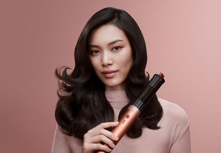 Modelka z ciemnymi włosami używa multistylera Dyson Airwrap Coanda2x do kręcenia loków. Wersja mobile.