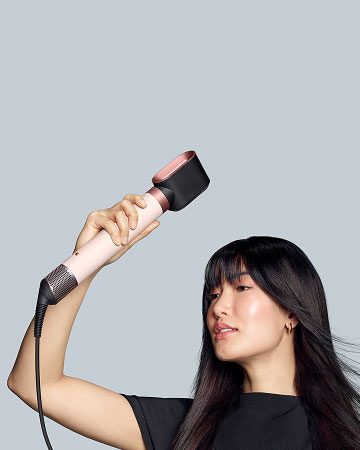 Modelka z ciemnymi włosami trzyma w ręku multistyler Dyson Airwrap Coanda2x  z końcówką do suszenia. Wersja mobile.