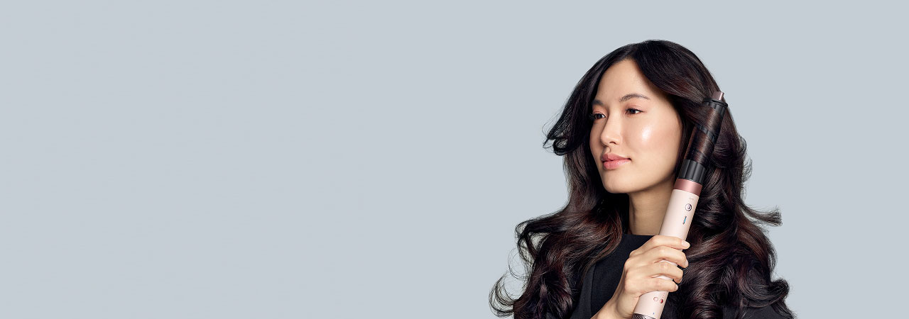 Modelka z ciemnymi włosami kręci loki używając multistylera Dyson Airwrap Coanda2x z końcówką cylindryczną.