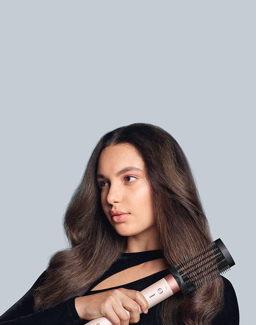 Modelka o brązowyach włosach czesze pasmo przy pomocy multistylera Dyson Airwrap Coanda2x. Wersja mobile.