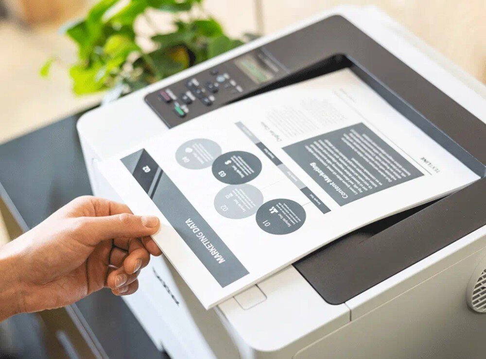 Drukarka BROTHER HL-L5210DW zbliżenie na wydruki wychodzące od góry z drukarki, dłoń chwytająca karki rozdzielczość prędkość druk dwustronny
