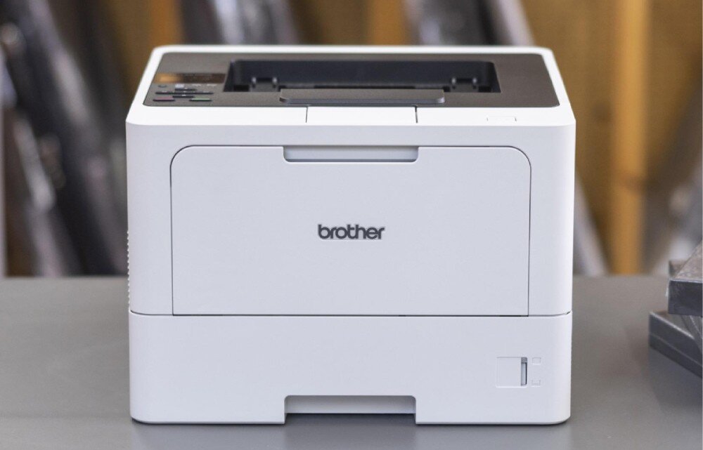 Drukarka BROTHER HL-L5210DW drukarka stojąca na stole przodem, rozmazane biuro w tle podajnik papieru taca odbiorcza pojemność