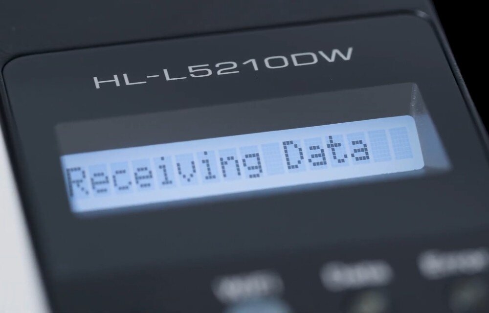 Drukarka BROTHER HL-L5210DW zbliżenie na wyświetlacz LCD drukarki, nazwa modelu napisana powyżej, na ekranie napis odbieranie danych łączność Wi-Fi obsługa podłączenie