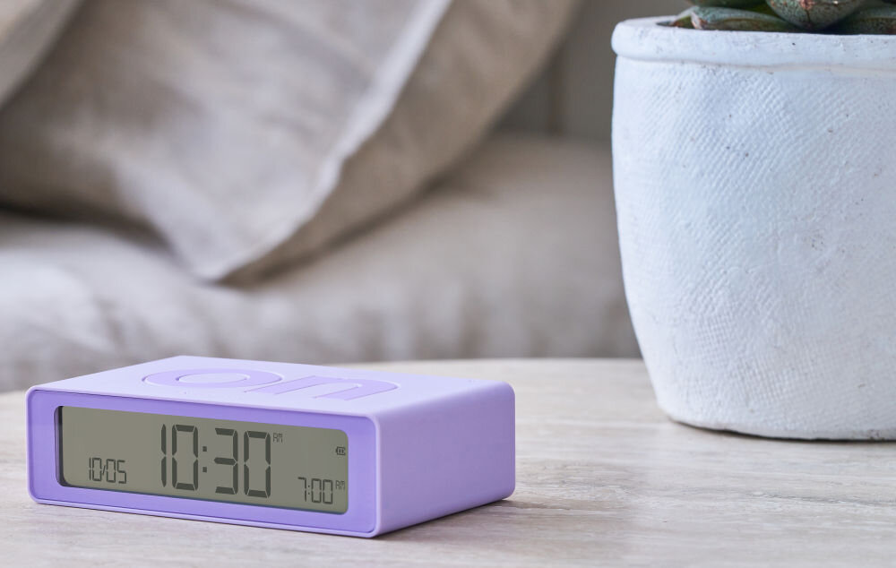 Budzik LEXON Flip Mini liliowy, podróż, USB-C, bateria, ekran, Klasyczny Lexon Flip Mini z napisem „off”, matowa grafitowa obudowa, jasny blat, wyraźny ekran.