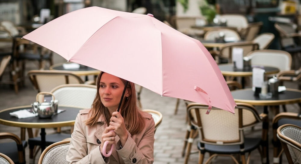 Parasolka LEXON Mini Hook LU21LP jasnoróżowy, lekkość, funkcjonalność, ABS, aluminium, kobieta trzyma parasolkę oburącz siedząc na krześle przy restauracji