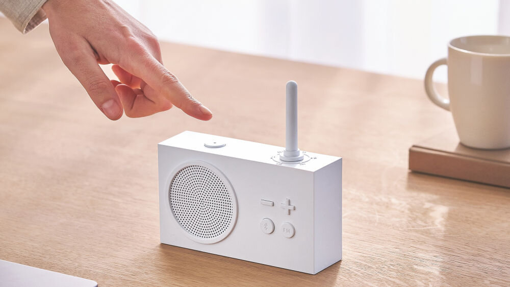 Radioodtwarzacz LEXON Tykho 3 biały, design, matowe wykończenie, styl, minimalizm, Palec dotyka przycisku na radiu Lexon Tykho 3, panel z głośnikiem, filiżanka w tle.