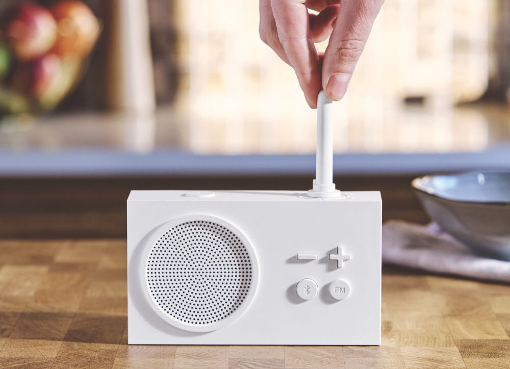 Radioodtwarzacz LEXON Tykho 3 biały, radio, Bluetooth, głośnik, funkcjonalność, Ręka obraca gumową antenę radia Lexon Tykho 3, widok z przodu, blat kuchenny, przyciski sterujące.