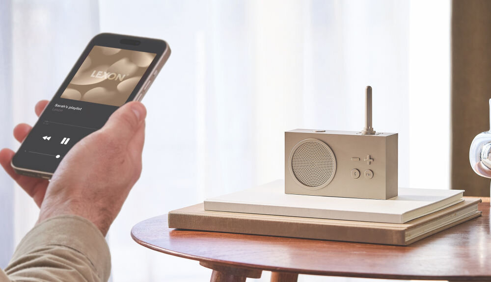 Radioodtwarzacz LEXON Tykho 3 złoty, mobilność, ABS, panel, sterowanie, Smartfon z aplikacją muzyczną, radio Lexon Tykho 3 łączy się przez Bluetooth na tle jasnego okna.