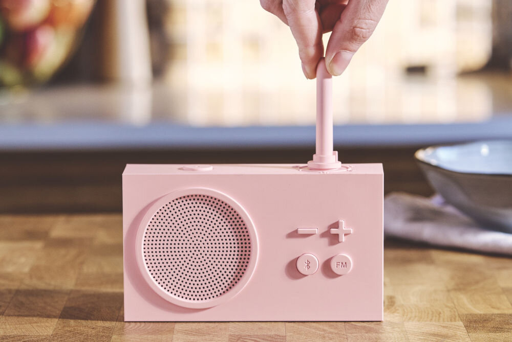Radioodtwarzacz LEXON Tykho 3 różowy, radio, Bluetooth, głośnik, funkcjonalność, Ręka obraca gumową antenę radia Lexon Tykho 3, widok z przodu, blat kuchenny, przyciski sterujące.