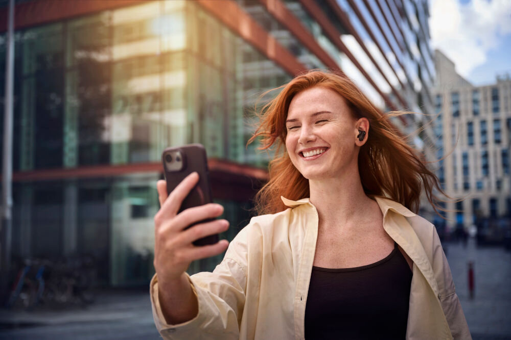 Słuchawki dokanałowe PHILIPS TAT6000BK/00 ciepłe brzmienie naturalny dźwięk szczegółowy bas, osoba z założonymi słuchawkami dokanałowymi trzymająca smartfon w ręku