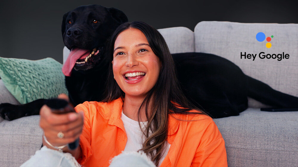 Telewizor SHARP 75JP7765E Asystent Google sterowanie głosem, osoba siedząca przed kanapą z psem trzymająca pilot w ręku