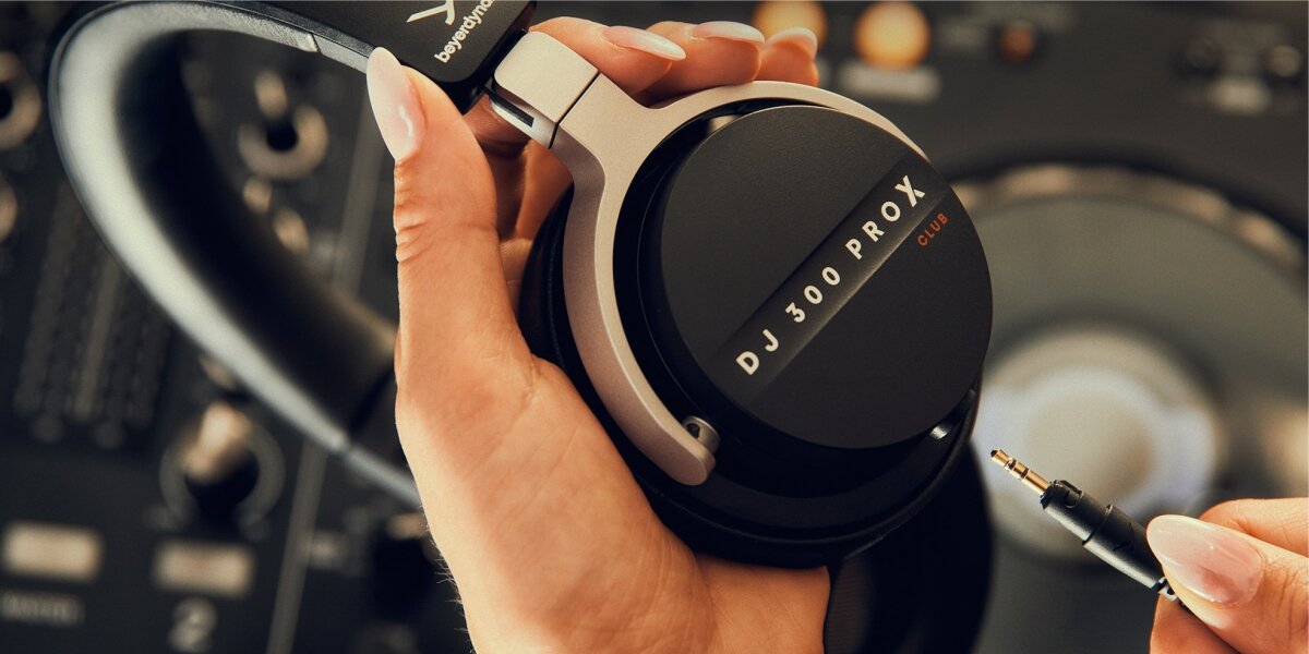 Słuchawki nauszne BEYERDYNAMIC DJ 300 Pro X Club - Dźwięk w pełnej głębi, osoba trzymająca słuchawki w ręku, podpinająca kabel jack
