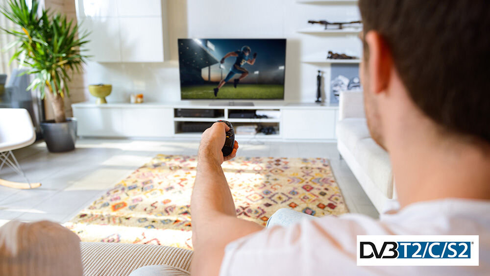 Telewizor JVC LT-55VGQ750P tuner DVB-T2 C S2 HEVC obraz, osoba siedząca na kanapie z pilotem w ręku