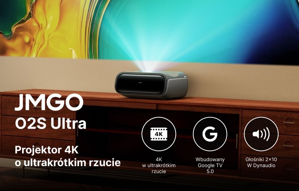 Na drewnianej szafce stoi projektor emitujący niebieskie światło na ścianę z kolorową grafiką. Obok projektora widnieje tekst: \'JMGO O2S Ultra Projektor 4K o ultrakrótkim rzucie\', a poniżej ikony z napisami: \'4K w ultrakrótkim rzucie\', \'Wbudowany Google TV 5.0\', \'Głośniki 2x10 W Dynaudio\'.