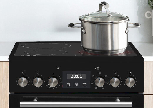 Zbliżenia na płytę ceramiczną i pokrętła kuchenki elektrycznej MPM-55-KEC-41. Na płycie garnek z pokrywką.