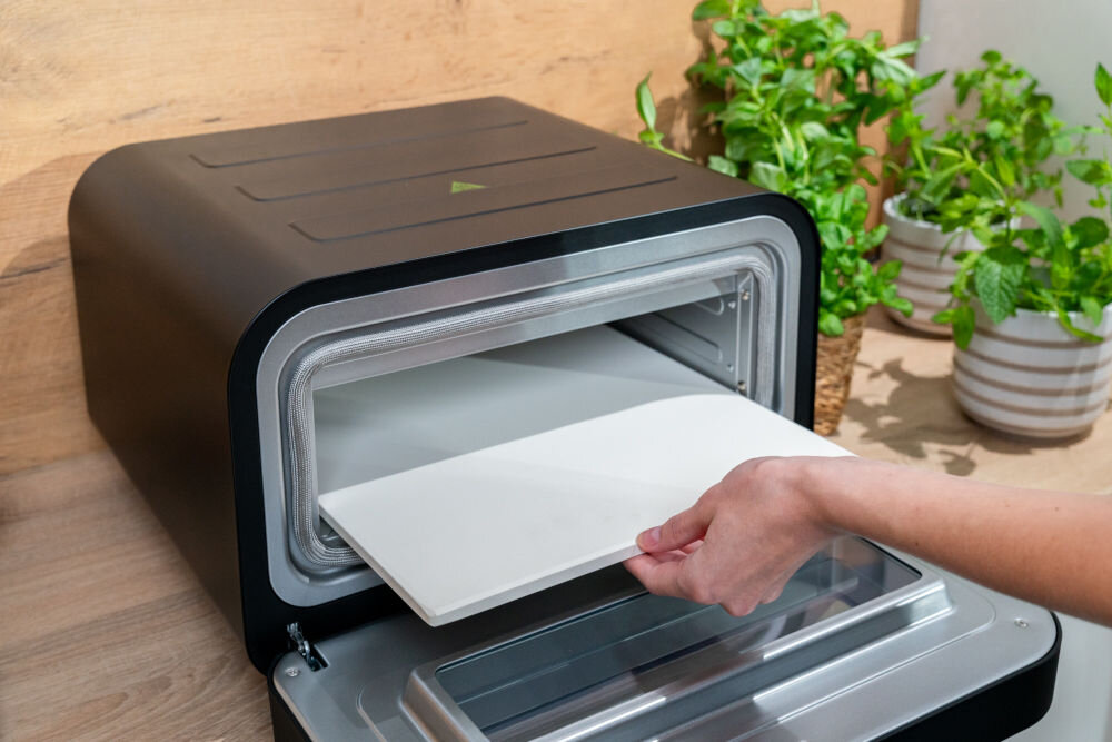 Piec do pizzy GÖTZE & JENSEN PO400K 1700W średnica 32 cm kamień do pieczenia i łopatka w zestawie Czarny piec na białym tle widoczny od przodu pod skosem wymiary 32 × 32 cm do pizzy o średnicy do 30 cm ciasto wypieka się równomiernie pizzy z pieca opalanego drewnem