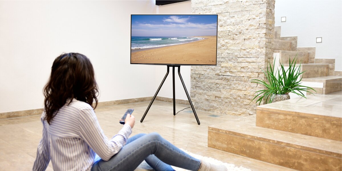 Stojak podłogowy HAMA do TV 37-75 cali 220872 Czarno-brązowy Salon w jasnych barwach z telewizorem na czarnym statywie trójnogu, prezentujący minimalistyczny design wnętrza.