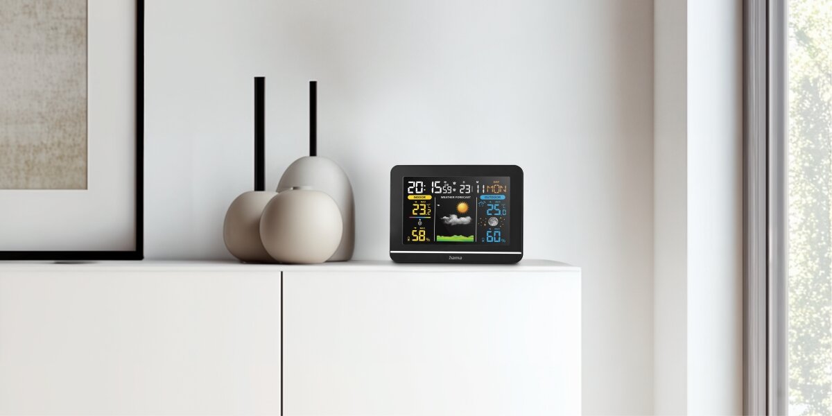 Stacja pogodowa HAMA Usedom Czarny Cyfrowa stacja pogodowa Hama z kolorowym wyświetlaczem stojąca na białej komodzie w nowoczesnym salonie.