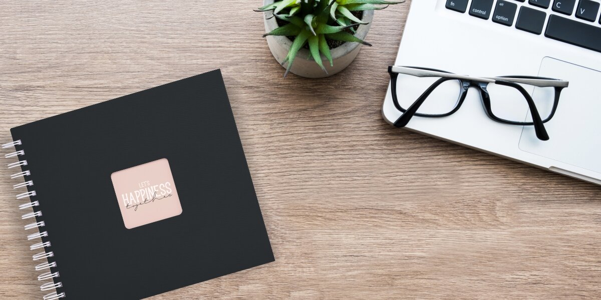 Album HAMA Fine Art 9831 Czarny (50 stron) Czarny album fotograficzny z napisem Let's Happiness Together na biurku obok laptopa, okularów i rośliny.