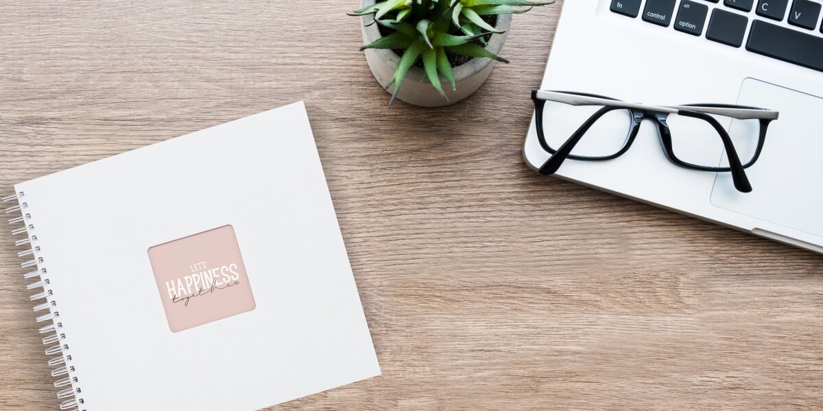 Album HAMA Fine Art 9844 Biały (50 stron) Biały album na zdjęcia w lnianej oprawie leżący na drewnianym biurku obok laptopa, okularów i rośliny doniczkowej