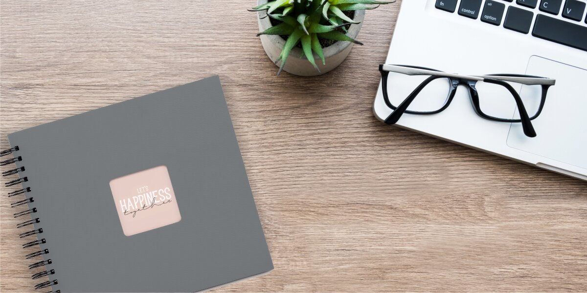 Album HAMA Fine Art 9841 Czarne kartki Szary (50 stron) Szary album fotograficzny z napisem Let's Happiness Together leżący na biurku obok okularów i laptopa.