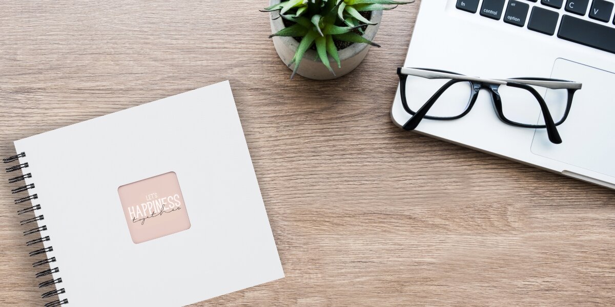 Album HAMA Fine Art Czarne kartki Biały (50 stron) Album fotograficzny Let's Happiness Together na drewnianym biurku obok laptopa, okularów i rośliny.