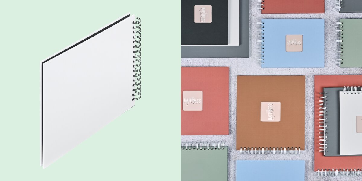 Album HAMA Fine Art Czarne kartki Biały (50 stron) Album fotograficzny na spirali zaprezentowany na tle kolorowej kolekcji albumów materiałowych.