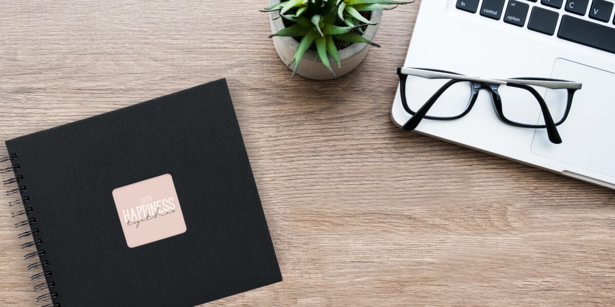 Album HAMA Fine Art 9835 Czarne kartki Czarny (50 stron) Album fotograficzny Let's Happiness Together na drewnianym biurku obok laptopa, okularów i rośliny.