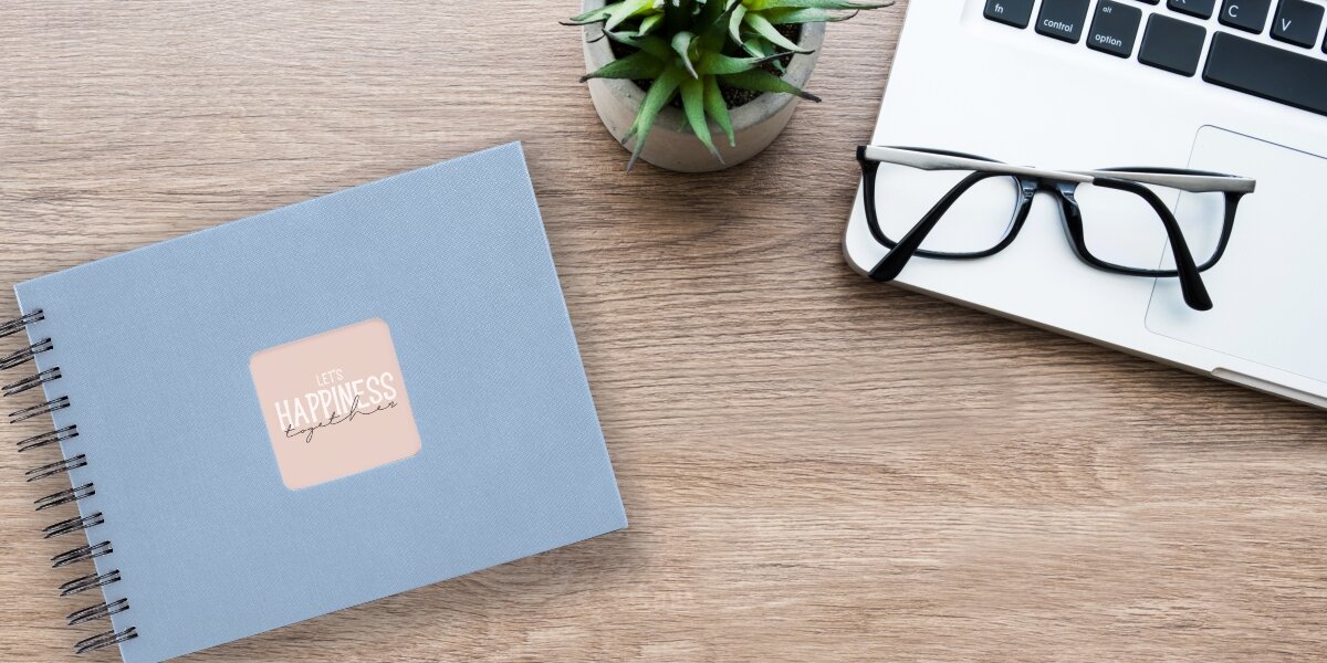 Album HAMA Fine Art Czarne kartki Błękitny (50 stron) Album fotograficzny Let's Happiness Together na drewnianym biurku obok laptopa, okularów i rośliny.