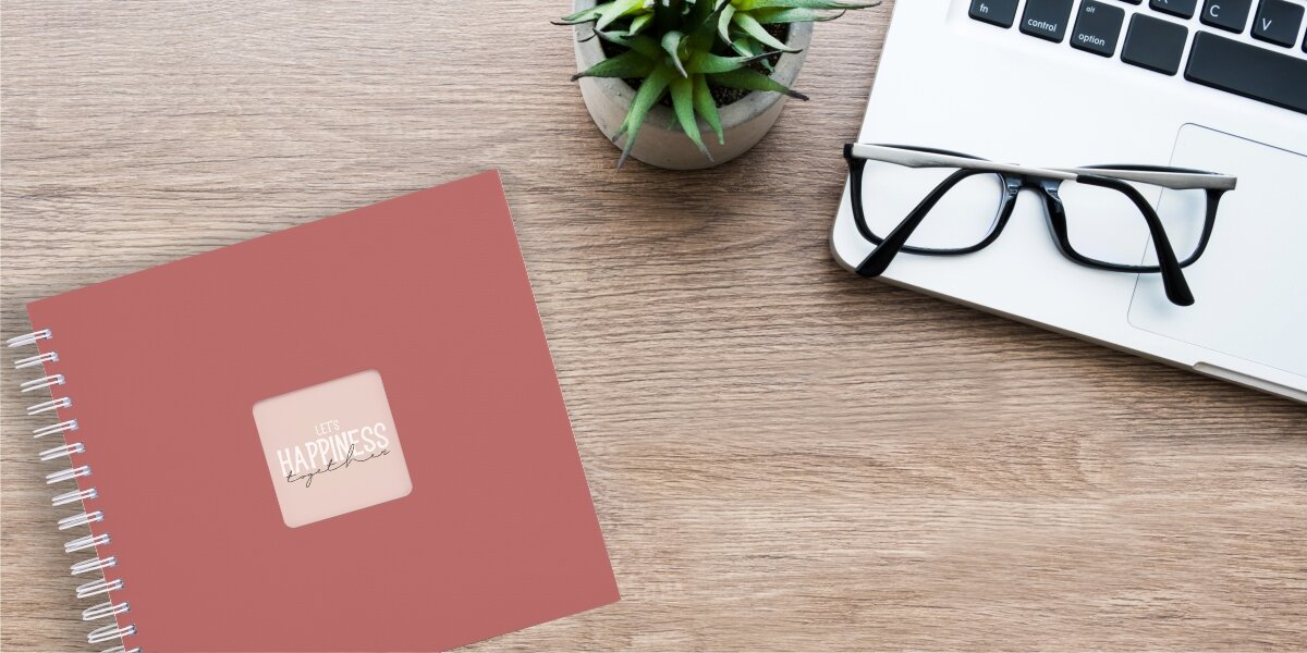 Album HAMA Fine Art Ceglany (50 stron) Album fotograficzny Let's Happiness Together na drewnianym biurku obok laptopa, okularów i rośliny.