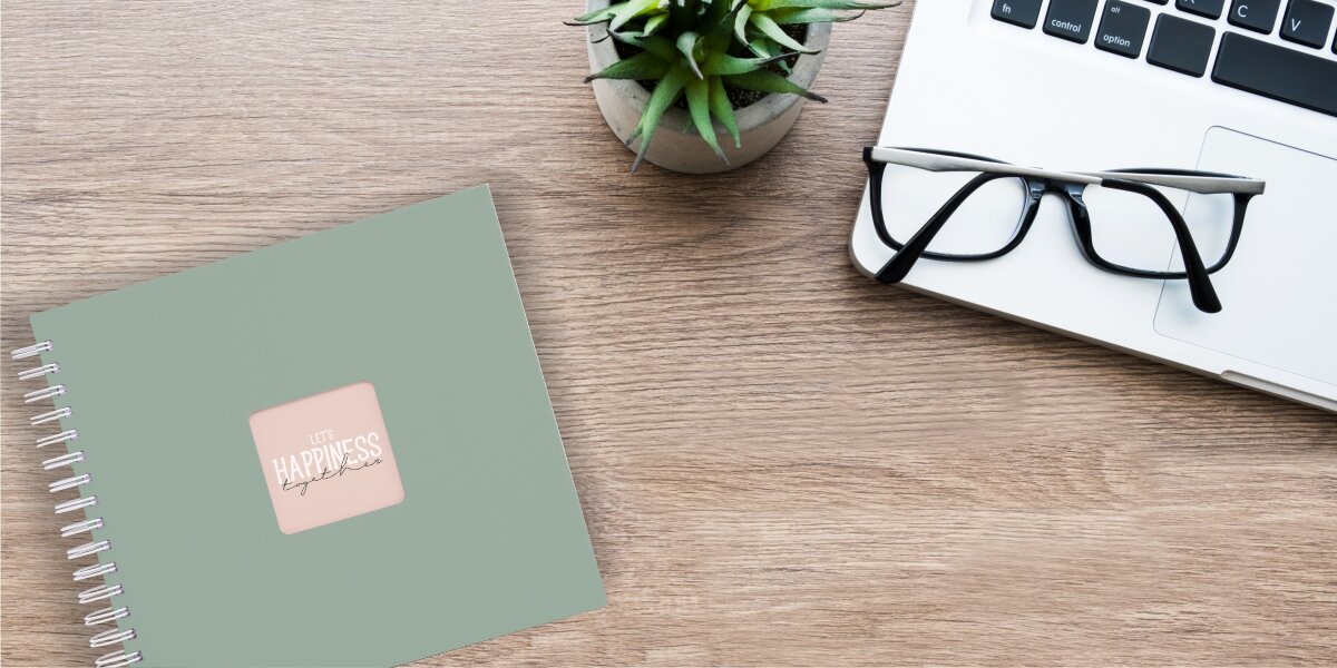 Album HAMA Fine Art 9867 Białe kartki Szarozielony (50 stron) Album fotograficzny Let's Happiness Together na drewnianym biurku obok laptopa, okularów i rośliny.