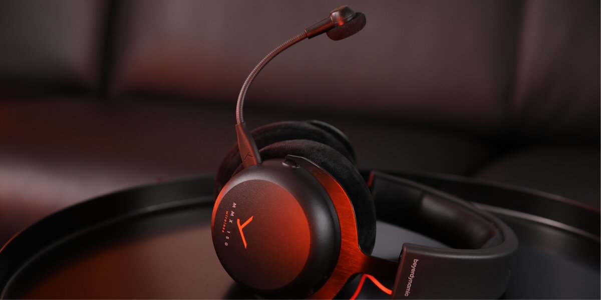 Słuchawki gamingowe beyerdynamic MMX 150 leżące na czarnej, okrągłej podstawce. Podświetlone na czerwono, uwydatniające logo MMX 150 Wireless i odpinany mikrofon na elastycznym pałąku. Scena w klimatycznym, zaciemnionym otoczeniu.