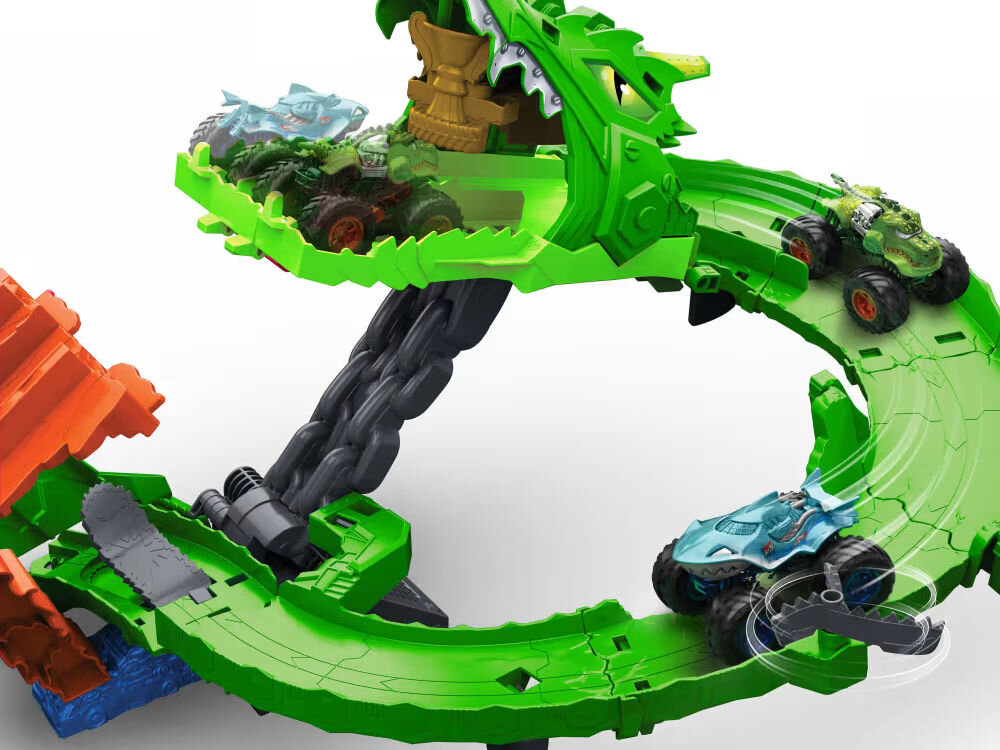 Samochód zdalnie sterowany Hot Wheels Tiger Shark HNV03 Zbliżenie na tor wyścigowy Hot Wheels Monster Trucks Dragon Arena w akcji. Dwa samochody monster truck (zielony dinozaur i niebieski rekin) poruszają się po zielonej pętli. Pasza smoka jest otwarta i wewnątrz widać inne samochody. Tło jest białe.