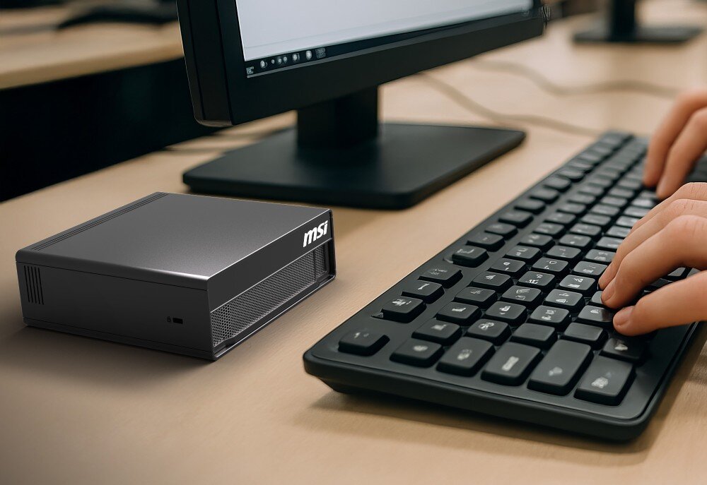 Komputer MSI EDGEXPERT-32SEU-BGB104TG5 Małe czarne urządzenie komputerowe stoi na biurku obok klawiatury i monitora, przy klawiaturze widać dłonie piszącej osoby, pamięć, przepustowość