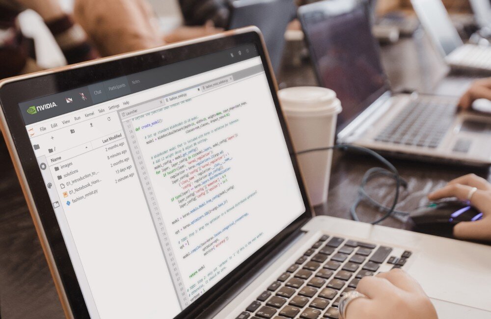 Komputer PNY DGXSPARK-FOUNEDIT-EU Zbliżenie na ekran laptopa, na którym otwarte jest środowisko do programowania z kodem w języku Python, a obok na biurku stoją inne laptopy i jednorazowy kubek, system, narzędzia, rozwiązania