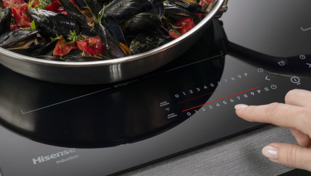 Płyta indukcyjna HISENSE HI8432BSCWF lifestyle panel dłoń palec patelnia danie sterowanie ustawienia regulacja funkcje panel suwak regulacja mocy suwaki sterowanie Wielostrefowe sterowanie precyzja komfort