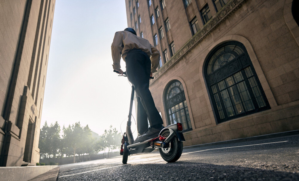 Hulajnoga elektryczna SEGWAY Ninebot F3 Pro D 70km 1200W Amortyzacja 10 cali Czarny miasto niebo budynki osoba jedzie na hulajnodze po ulicy środek codziennego transportu styl stabilność bezpieczeństwo