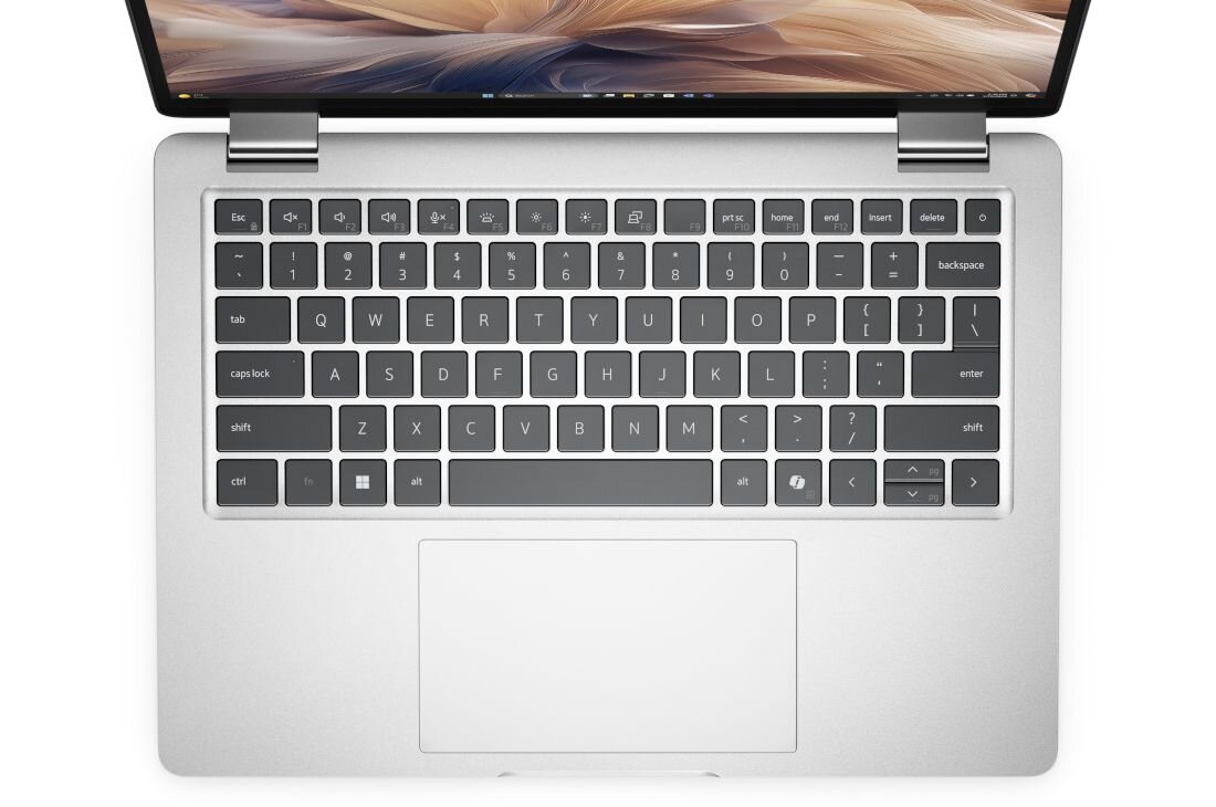 Obraz przedstawia klawiaturę laptopa z wyraźnie widocznymi klawiszami, w tym klawisze funkcyjne i alfanumeryczne. Laptop ma srebrną obudowę i duży touchpad poniżej klawiatury.