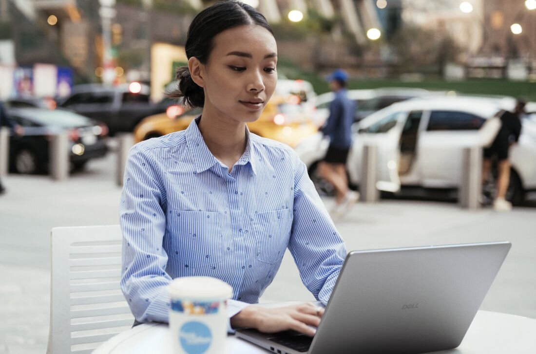 Osoba pracuje na laptopie DELL Pro 14 PC14250 z obsługą Wi-Fi 6E siedząc przy stoliku w miejskiej przestrzeni publicznej – Bluetooth pasma 2,4 GHz 5 GHz 6 GHz RJ-45 Gigabit Ethernet