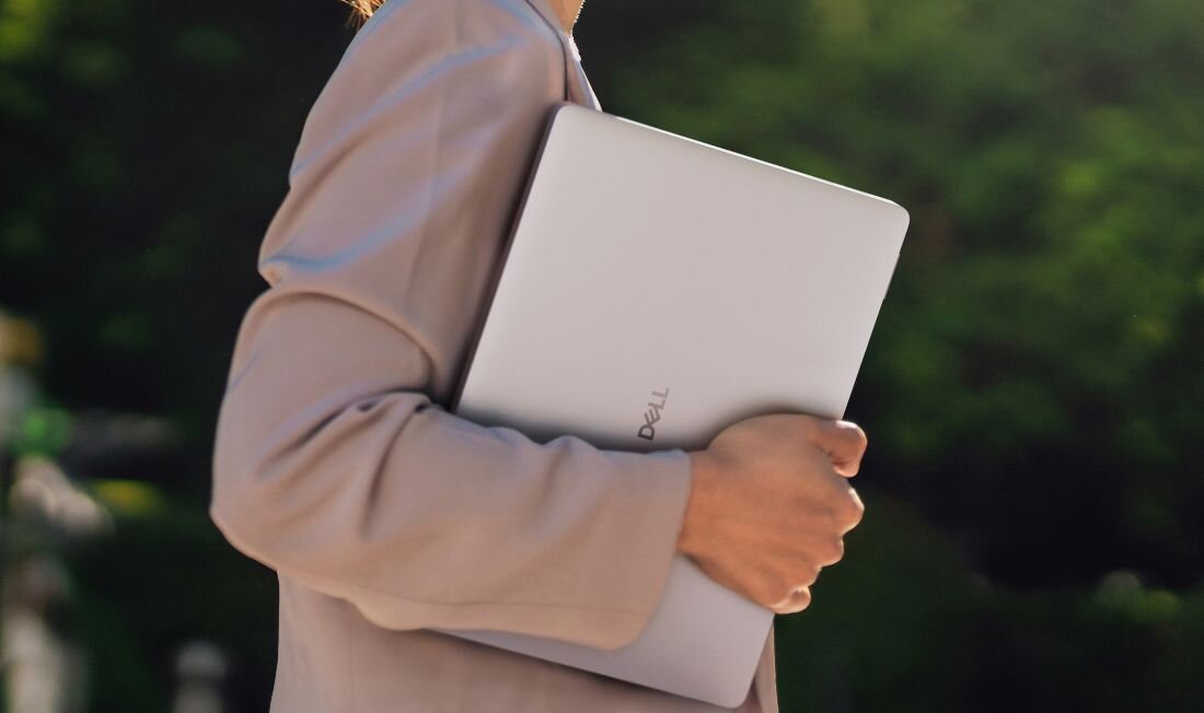 Osoba niesie laptopa DELL Pro 14 PC14250 pod pachą podczas spaceru na zewnątrz – certyfikat ENERGY STAR EPEAT Gold Climate+ TCO 9. generacji