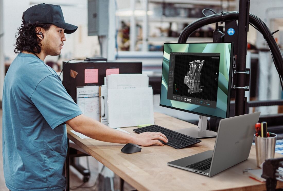Osoba pracuje przy biurku z komputerem stacjonarnym i laptopem. Na monitorze wyświetlany jest model 3D, a na laptopie widoczne jest logo DELL.