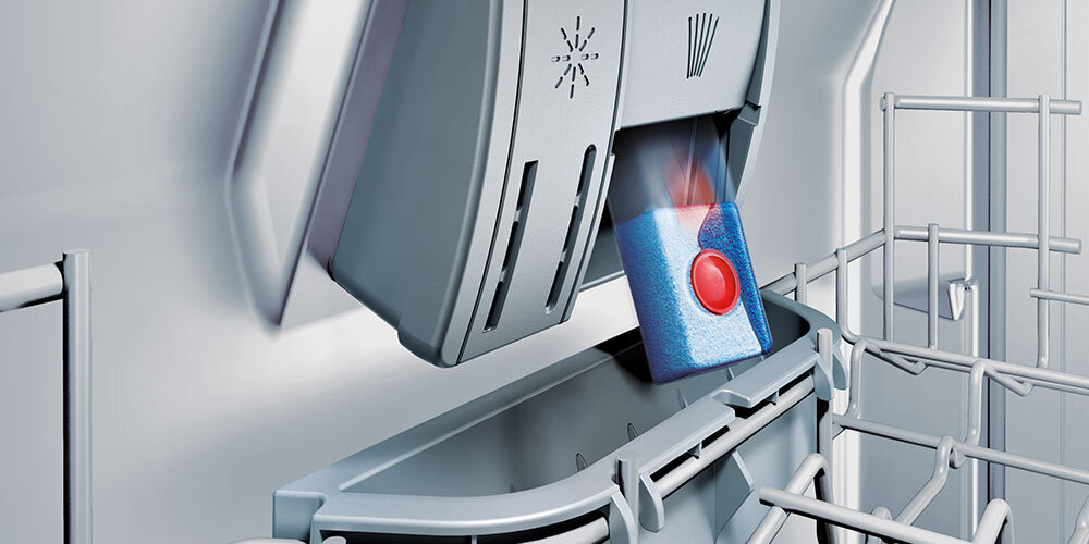 ZMYWARKA SIEMENS SN73EX06VE Na zdjęciu znajduje się grafika pokazująca przejrzysty uchwyt dozujący tabletkę czyszczącą wewnątrz zmywarki. Otwarta klapka dozownika sugeruje optymalne rozpuszczanie detergentu asystent dozowania optymalne wykorzystanie detergentu skuteczne zmywanie równomierne rozprowadzanie kapsułki
