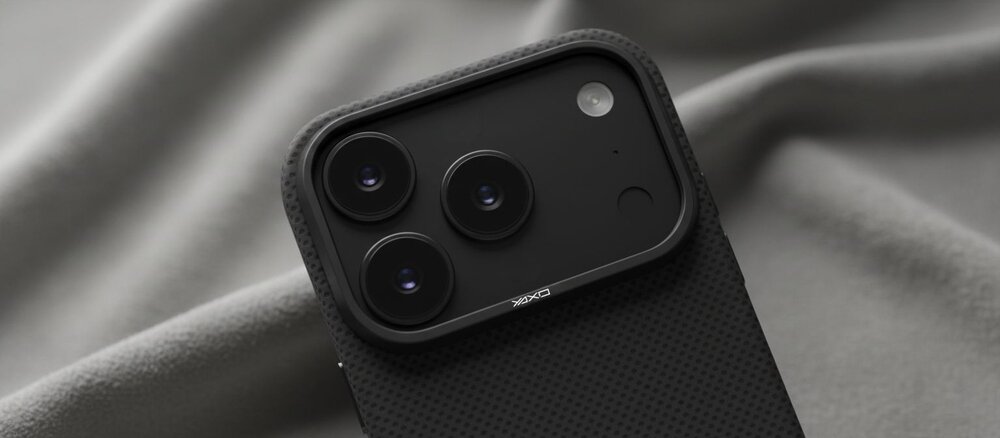 Zbliżenie na moduł trzech aparatów iPhone 17 Pro w czarnym etui YAXO z fakturą z włókna aramidowego, leżącego na miękkiej szarej tkaninie