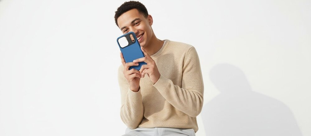 Uśmiechnięty mężczyzna w beżowym swetrze trzyma w dłoniach i ogląda niebieskie etui do iPhone 17 Pro Max.