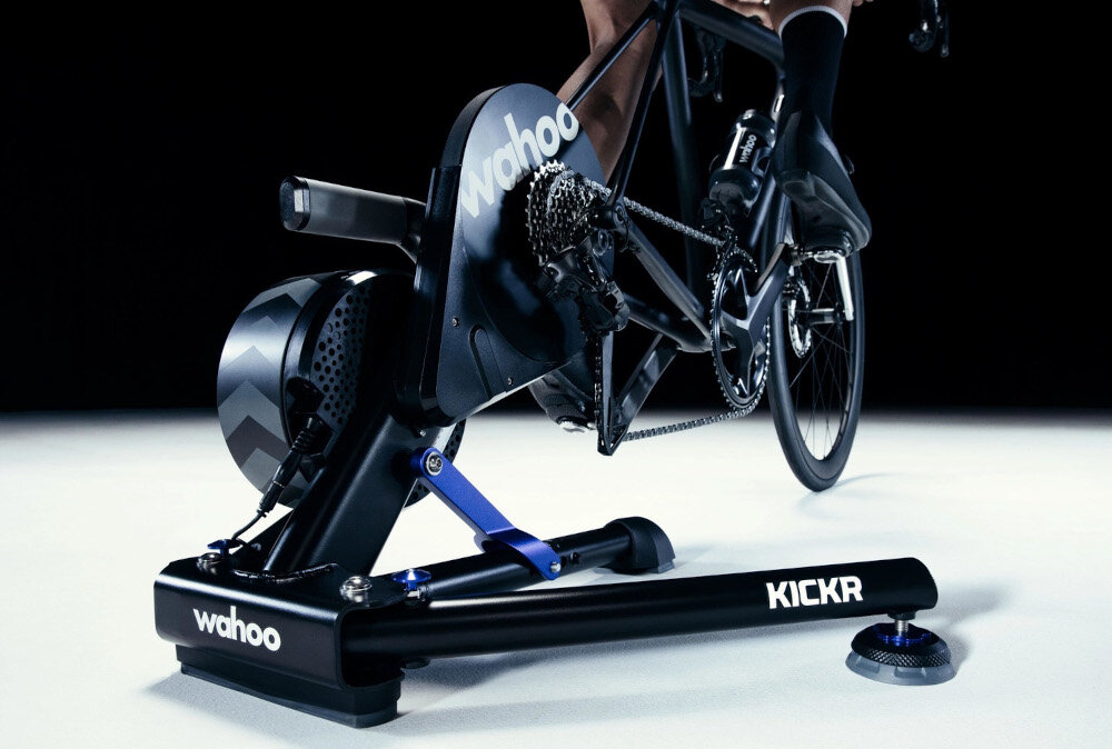 Trenażer rowerowy WAHOO Kickr Smart Trainer V6 WFBKTR122 ciemne tło osoba jedzie na rowerze rower umieszczony na trenażerze tryb ERG automatycznie dostosowuje opór odwzorowując różne nachylenia do 20% i zjazdy do -15% realistycznie odtworzyć warunki terenowe moc do 2200 W elektromagnetyczny układ napędowy