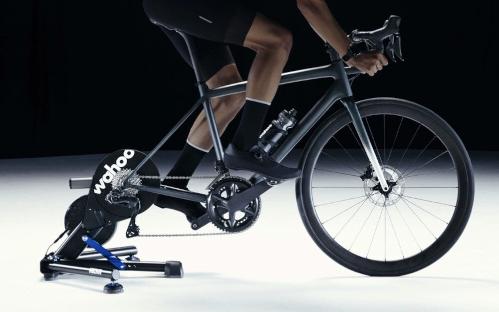 Trenażer rowerowy WAHOO Kickr Smart Trainer V6 WFBKTR122 ciemne tło osoba jedzie na rowerze rower umieszczony na trenażerze dokładność pomiaru mocy +/-1% automatyczna kalibracja rzetelne dane bez ręcznej ingerencji pomiar kadencji i mocy można śledzić postępy i optymalizować trening