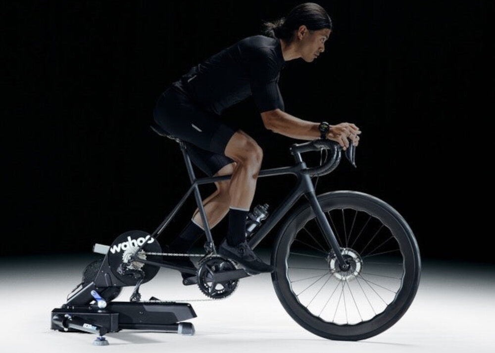 Trenażer rowerowy WAHOO Kickr Move Power Trainer WFBKTR123 ciemne tło osoba jedzie na rowerze rower umieszczony na trenażerze realistyczny trening trening rowerowy w domy wszechstronność wygoda bezpieczeństwo