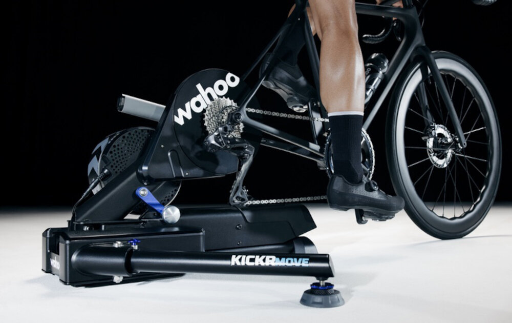 Trenażer rowerowy WAHOO Kickr Move Power Trainer WFBKTR123 ciemne tło osoba jedzie na rowerze rower umieszczony na trenażerze trenażer rowerowy rolkowy tylne koło spoczywa na rolkach przednie w uchwycie stabilizującym odwzorowuje naturalne odczucia jazdy realistyczny trening w domu