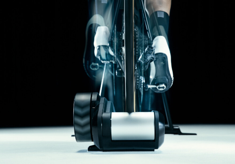 Trenażer rowerowy WAHOO Kickr Rollr Smart Trainer V2 WFBKTR9B ciemne tło osoba jedzie na rowerze rower umieszczony na trenażerze widok od tyłu system stabilizacji przedniego koła utrzymuje rower w odpowiedniej pozycji naturalne odczucie jazdy komfort ćwiczeń bezpieczeństwo